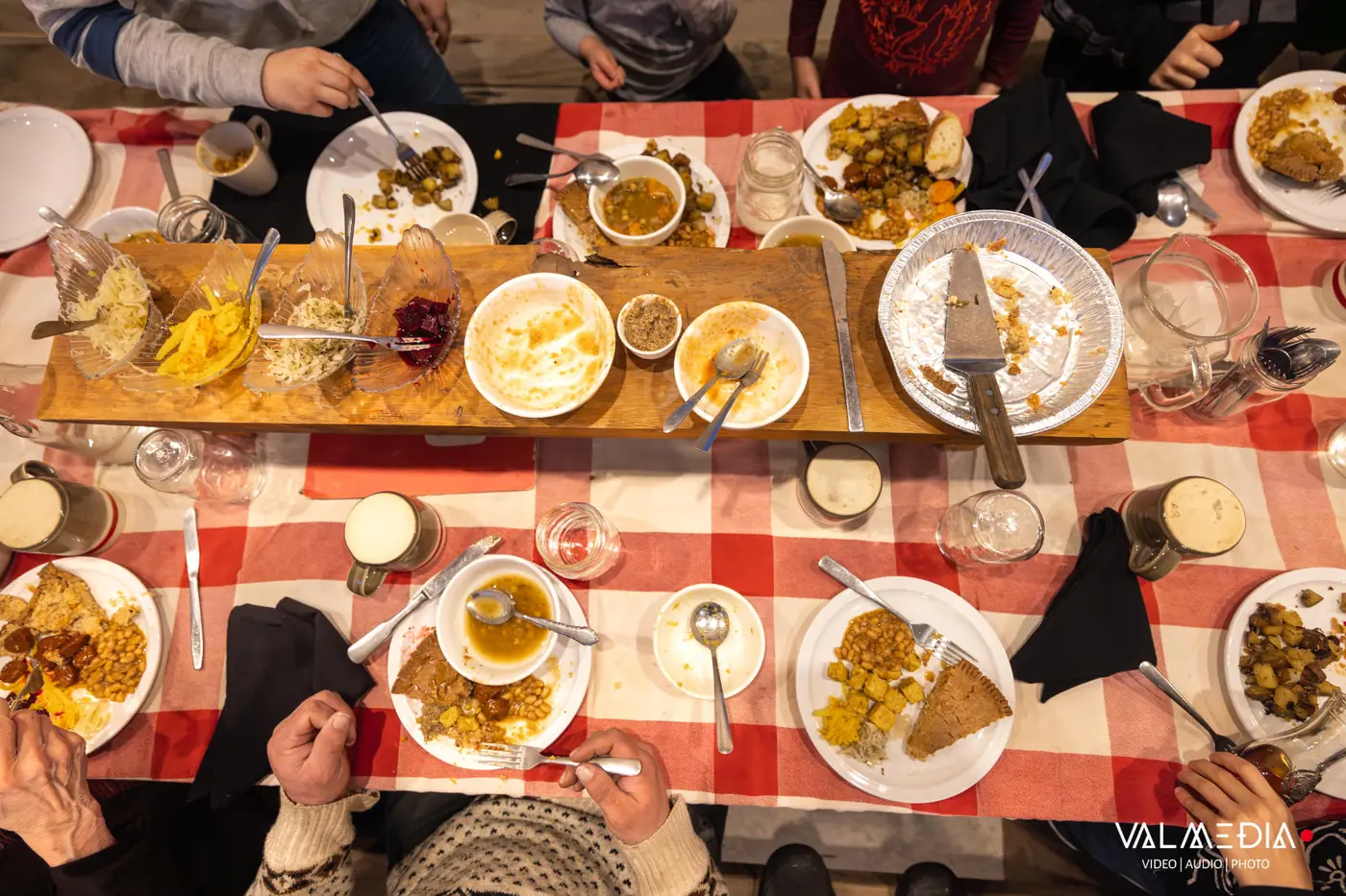 The full table seen from above: tourtière, beans, potatoes and soup on a red-and-white checkered tablecloth.